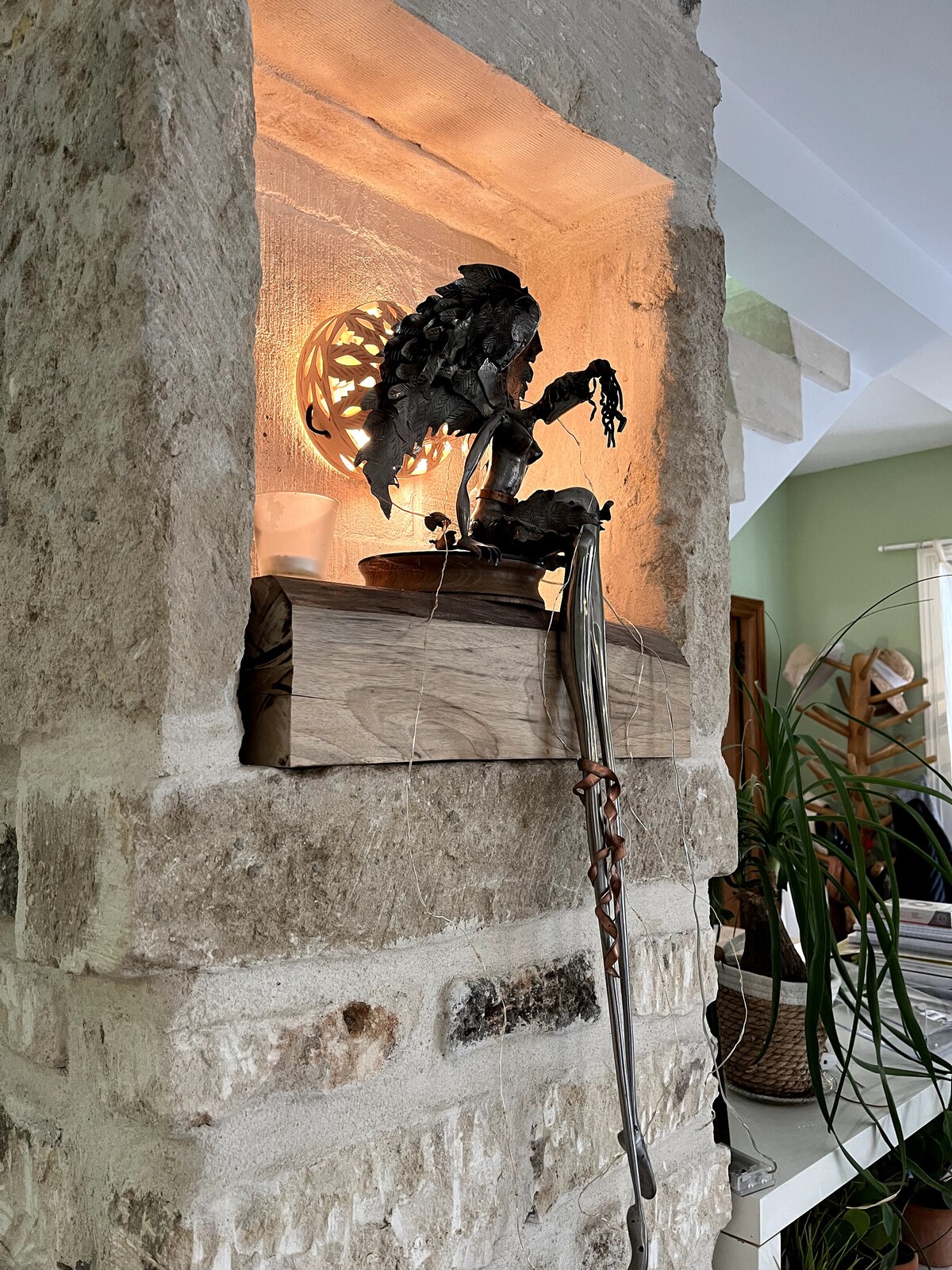 Alcôve décorative en pierre avec sculpture, lampe sphérique et objet métallique suspendu au mur.