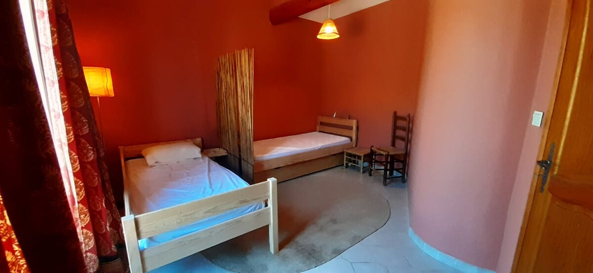 Chambre chaleureuse avec lits simples, murs rouges, lampe sur pied et séparation en bambou.