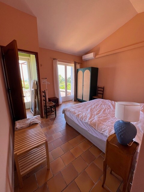 - Chambre lumineuse avec murs terracotta, lit blanc, armoire verte et accès à balcon arboré.