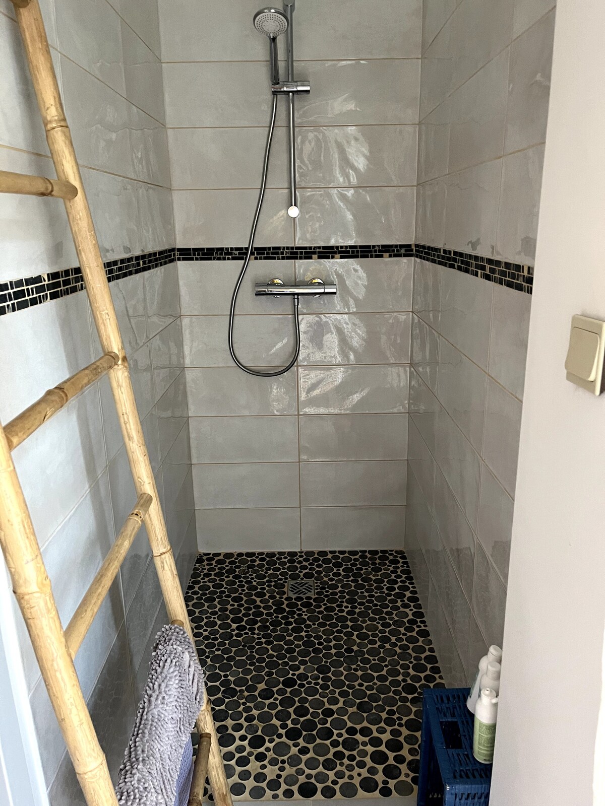 Douche contemporaine avec carrelage gris, bande mosaïque, sol en galets et échelle en bambou.
