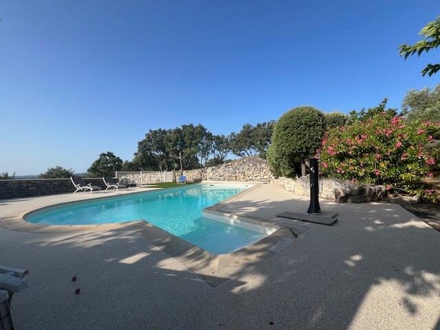 Grande piscine extérieure en L avec terrasse en pierre et douche solaire dans une location de vacances à Saint-Restitut.