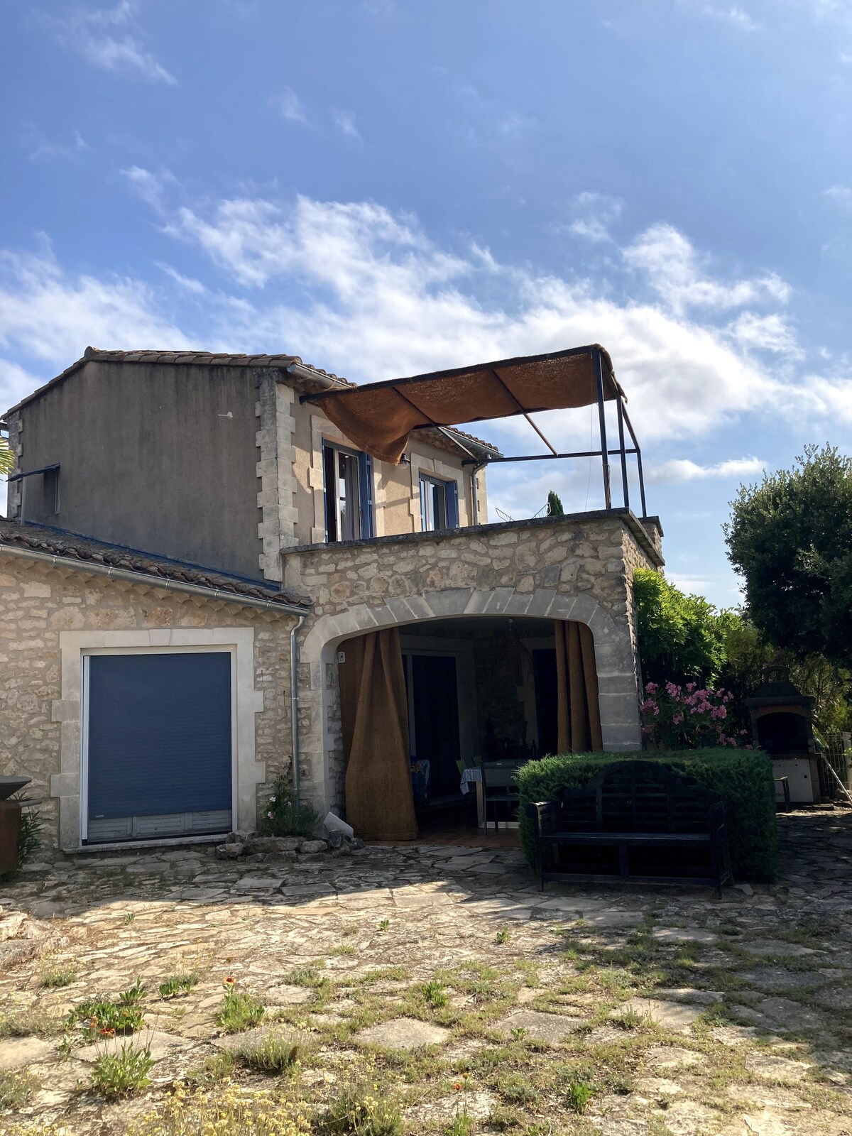 Maison en pierre à deux niveaux avec cour pavéd, banc, brasero et végétation fleurie