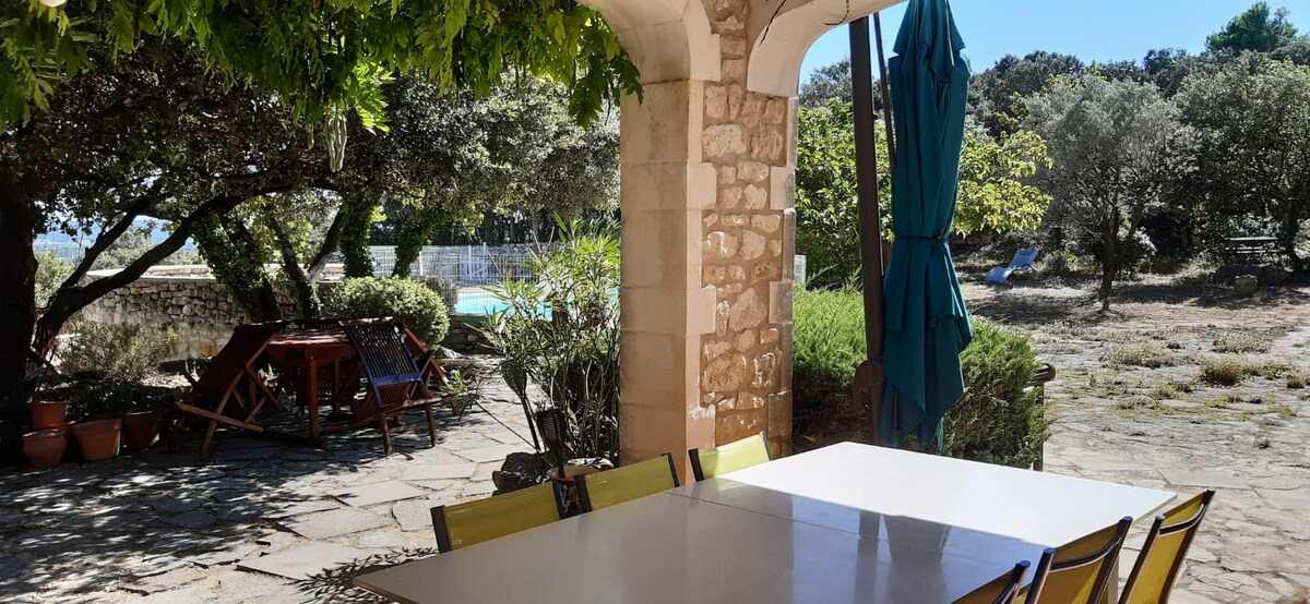 Patio ombragé avec arches en pierre, table blanche, chaises vertes et vue sur piscine.