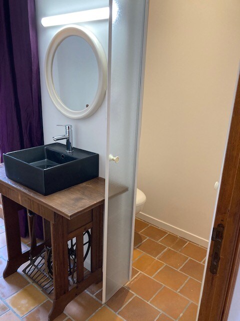 - Petit espace lavabo avec vasque noire sur meuble vintage, miroir rond et cloison en verre dépoli.