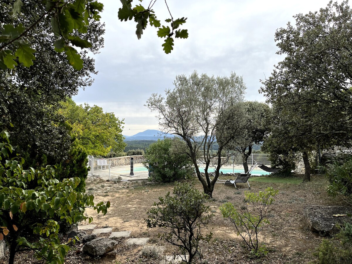 Piscine de la maison, entourée de jardin sec, arbres et vue sur collines.