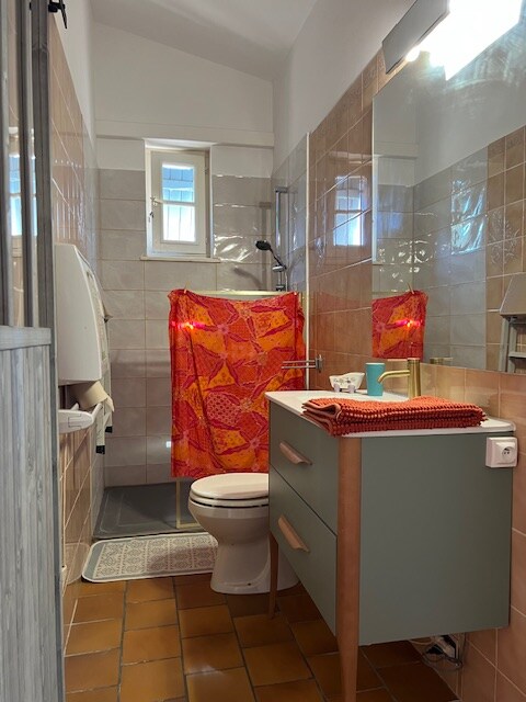 Salle de bain colorée avec meuble vert, rideau de douche rouge et carrelage beige.