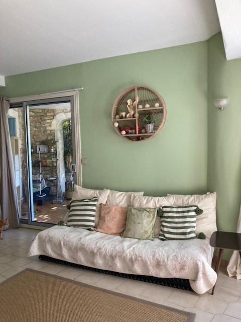 Salon cosy avec canapé blanc, coussins verts et roses, étagère ronde en bois et déco naturelle.