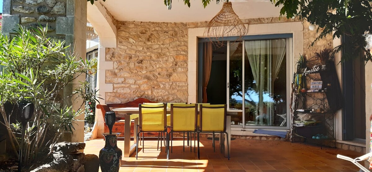 Terrasse en pierre avec table et chaises jaunes, devant maison en pierre et porte vitrée.